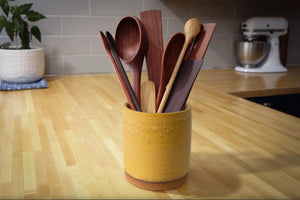 Set of wooden spoons in a yellow container on a kitchen counter.